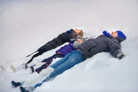 happy family poses on a snow glade, play and do snow angels? a close-knit cheerful family, parents together with the daughter, on the eve of a holiday of Christmasの写真素材