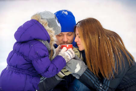 happy family poses on a snow glade, in hands of a circle of hot tea, a close-knit cheerful family,...