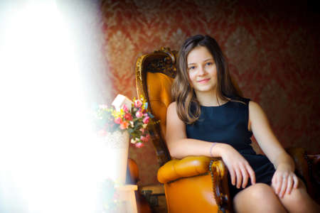 beautiful girl smiles and poses, sits on a chair, tulle at a window sideways develops on wind,...