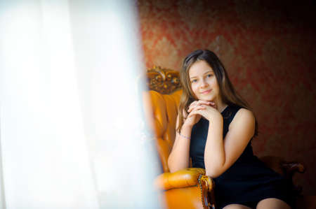 beautiful girl smiles and poses, sits on a chair having leaned on an elbow, tulle at a window...