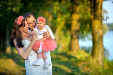 happy family walks in the park, together embrace and play with the daughter, on a background a bright sunsetの写真素材