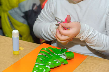 Children at a lesson of the fine arts, make gifts for a holiday of Christmas and new year. Cut out and stick together hand-made articles from color sheets of paper. Preparation for a holiday.の写真素材
