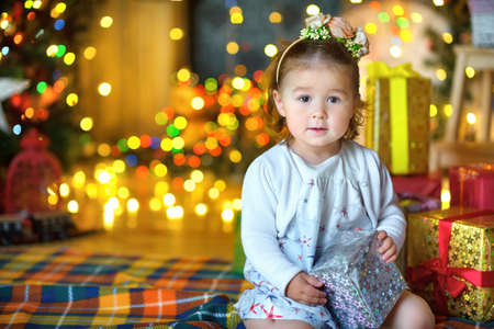 beautiful little girl, sits on a floor with a gift in hands, in a festive interior. A set of bright...