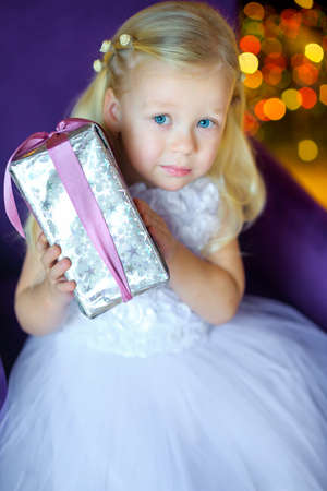 Girl in a beautiful long dress, sits on a chair with a gift in hands. On a background a set of bright sparksの写真素材