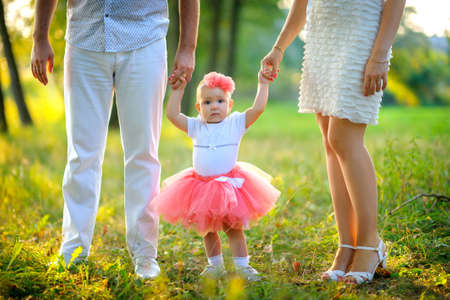 happy family walks in the park, parents hold the little daughter by hands, she smiles and looks in the cameraの写真素材