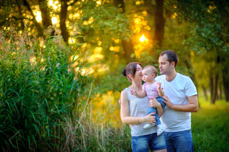happy family walks in the park, together embrace and play with the daughter, on a background a...
