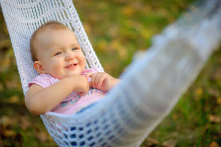 happy little girl in the park at the river, shakes on a hammock and smilesの写真素材