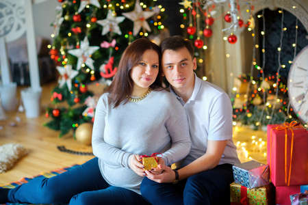 Happy young family waiting for the child's birth, in a festive interior, embrace and give gifts. Waiting for a holiday.の写真素材