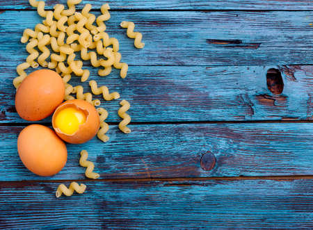 cooking, several eggs and macaroni lie on a wooden tableの写真素材