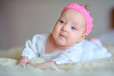 happy newborn baby lies on a chair in a beautiful pink knitted crown, with interest looks in the...