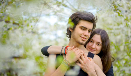beautiful girl gently embraces the guy, standing in the blossoming spring parkの写真素材