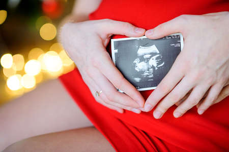 Pregnant mother holds the first picture of the kid near a tummyの写真素材