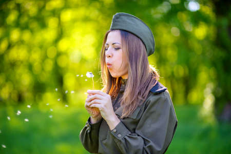 woman the military in the beautiful spring park at sunset with a dandelion in handsの写真素材