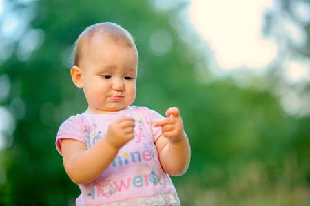 lovely kid in the evening outdoors, with interest considers a blade, a saturated green background