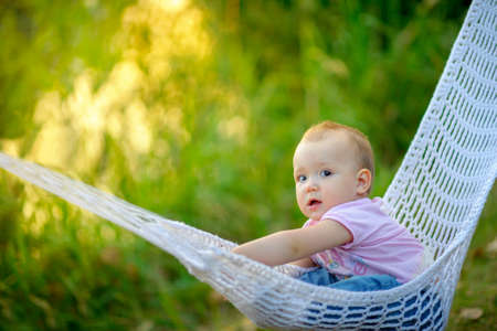 beautiful kid, lies in a hammock outdoors, with surprise looks in the camera, a bright evening sunsetの写真素材