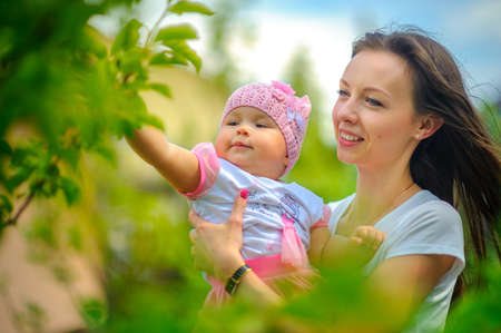 happy mother walks with the child in the park in sunny day, touch and consider leaves on a treeの写真素材