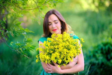 beautiful girl in a green dress with a big bouquet of flowers in the evening parkの写真素材