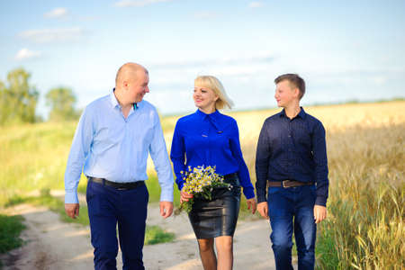 happy family walks near the field of ripe wheat, mother holds a bouquet of wild flowers in hand