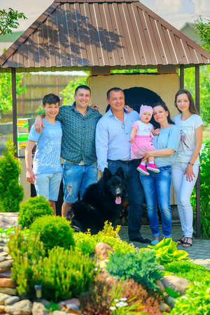 A large family, standing near their house, hugs and smile, next to them sits a dogの写真素材