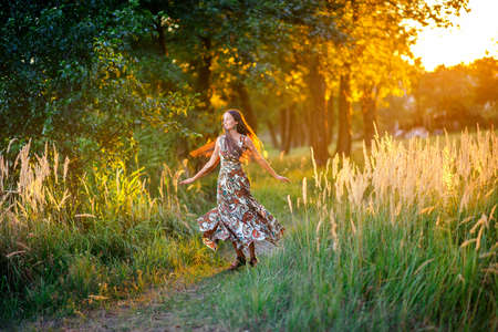 beautiful young girl walks in the park on a sunset, dances and has fun, the long dress beautifully developsの写真素材