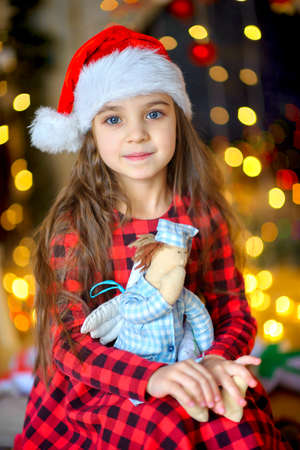 beautiful girl in santa claus cap sits on the floor against the bright festive garlandsの写真素材
