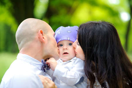 happy family walking in the park, parents hugging and kissing their babyの写真素材