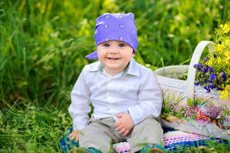 cheerful beautiful baby in evening park, sitting on grass and smiling