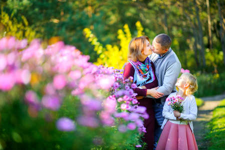 happy family walking in beautiful evening park, girl holding bouquet of flowers and looking at parentsの写真素材
