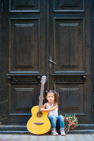 Beautiful little girl with a guitar, sits on the doorstep of a house near an old door