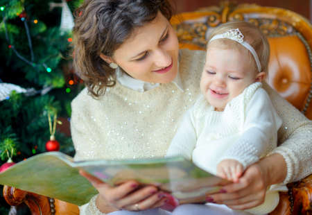 mother reads her daughter's tales, sitting near a festive Christmas tree