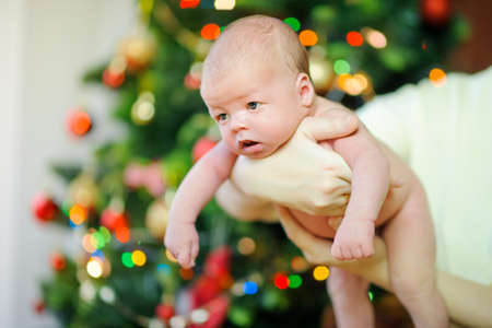 mother holding a newborn baby in the arms of a festive Christmas treeの写真素材
