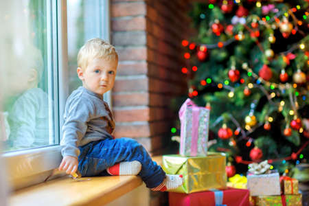 the beautiful kid sits and plays near a window, near a festive Christmas tree and set of giftsの写真素材