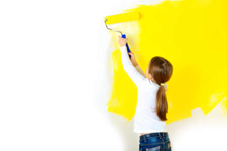 Beautiful girl paints a roller against a wall in a room, repairs in the houseの写真素材
