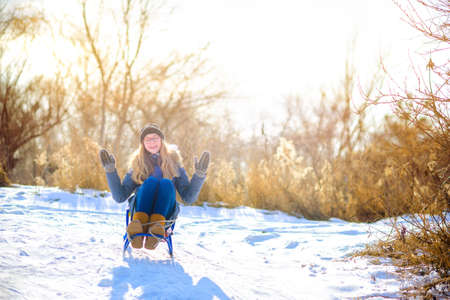 happy teen girl sledding in the park at sunset, laughing and having fun