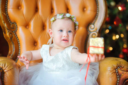 little girl in a dress sitting on the couch holding out a giftの写真素材