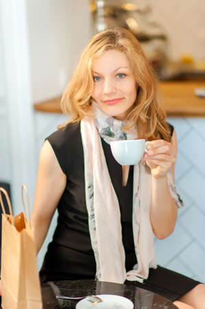 A girl who has made a purchase sits at a table in a bar and drinks coffeeの写真素材