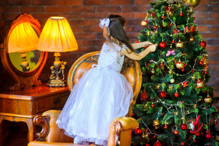 little girl in a dress decorates with balls festive Christmas treeの写真素材