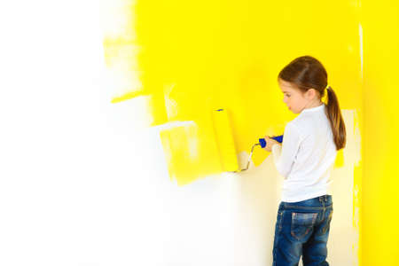 a little girl paints painfully the walls with a roller in the roomの写真素材