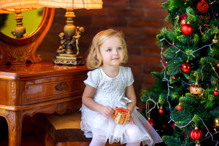 beautiful little girl near festive christmas tree holding gift in hands and smilingの写真素材