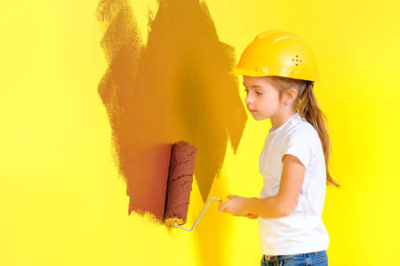 little girl in a construction helmet paints the wall with a roller, repairs in the house