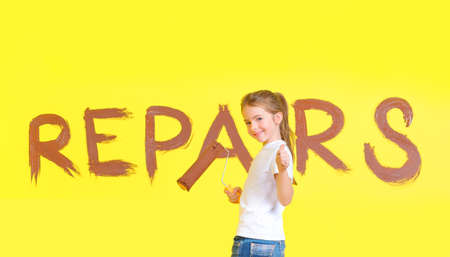 little girl with a roller for painting in her hands, stands near the painted wall with the words...