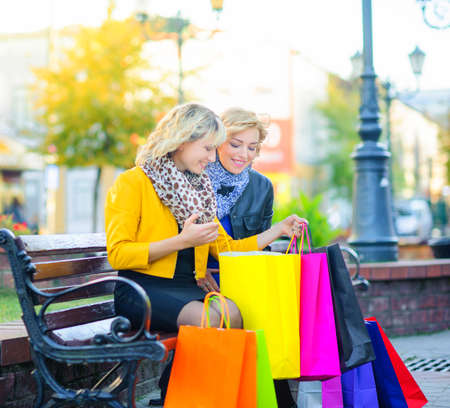 two girls sitting on a bench with packages are considering shoppingの写真素材