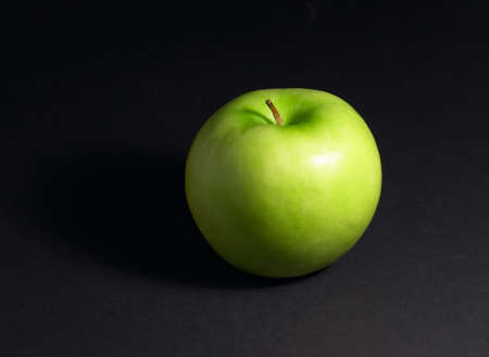 Green apple on black background with small shadowの写真素材