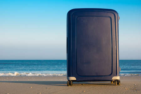 A blue suitcase on an empty beach with a quiet waterline and hardly any wavesの写真素材