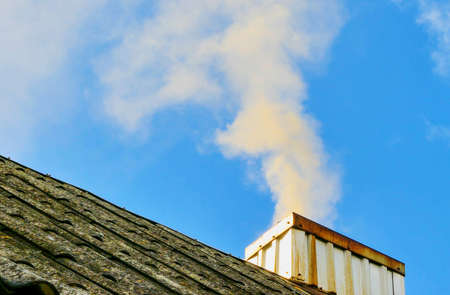 smoke rises from the chimney up against a background of blue skyの写真素材