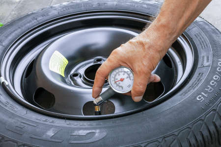 own garage Lithuania August 20-2020, the driver measures the pressure in a new tire with a manometerのeditorial素材