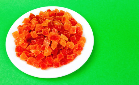 a bunch of candied papaya pieces on a plate on a light green background with space for textの写真素材