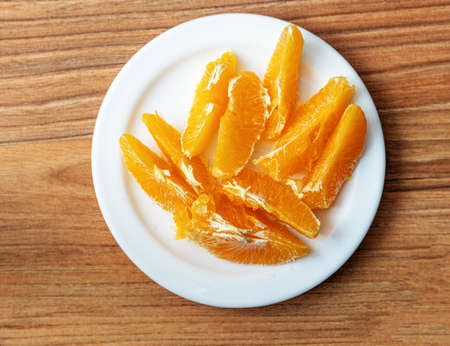 Cut oranges in a pile on a white plate on a pine table, top view