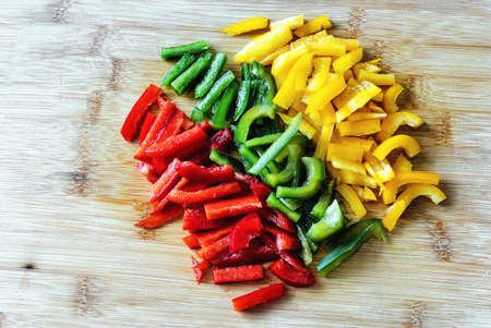 Top view of three colored red, green and yellow peppers, chopped on a cutting boardの写真素材
