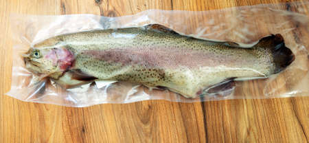 Rainbow trout in a transparent vacuum plastic bag on the surface of a pine tree table, top view